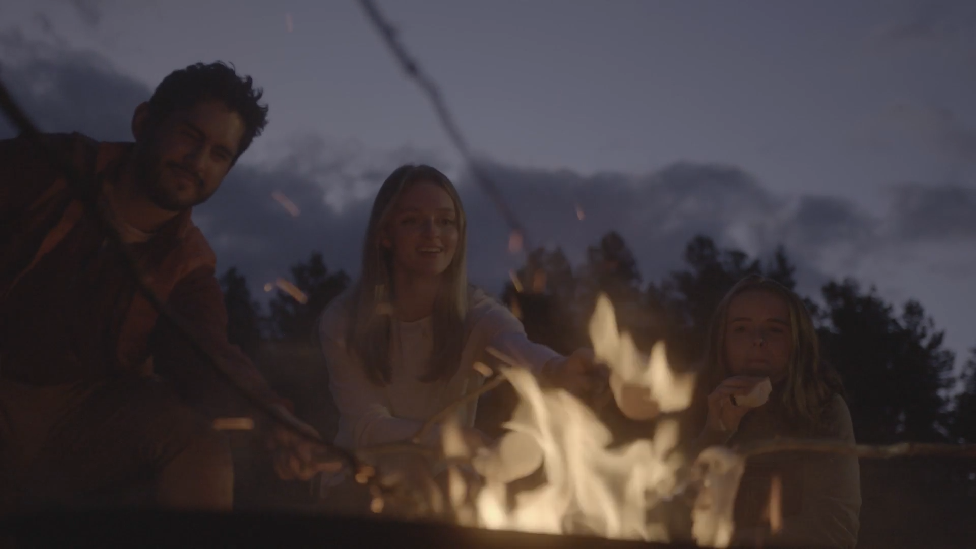 three students gathered around campfire